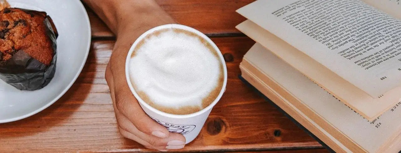 Person holding coffee cup and book