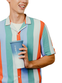 A man wearing a short-sleeve button-up shirt with vertical stripes in teal, orange, light blue, white, and lavender, holding a blue-to-white gradient travel tumbler cup.