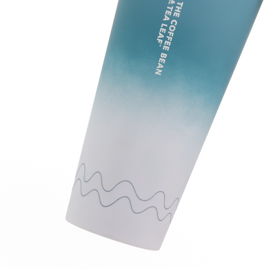 A close-up of a plastic travel tumbler showing a blue-to-white gradient design with vertical white text reading 'THE COFFEE BEAN AND TEA LEAF' near the top, plus a thin wavy line near the bottom, on a white background.