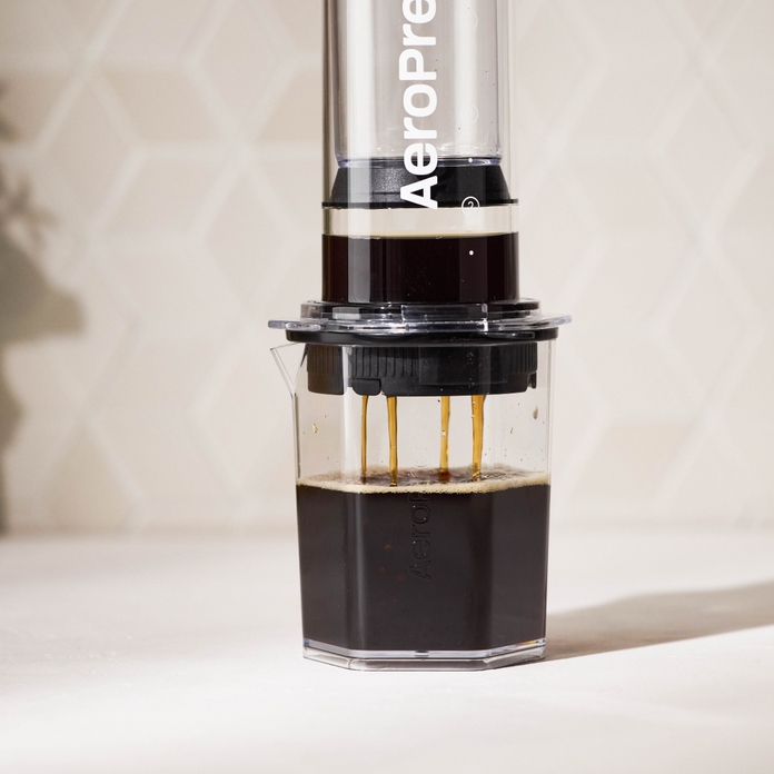 AeroPress coffee press with coffee being brewed on a light background