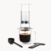 AeroPress coffee press with glass carafe and black scoop on a white background