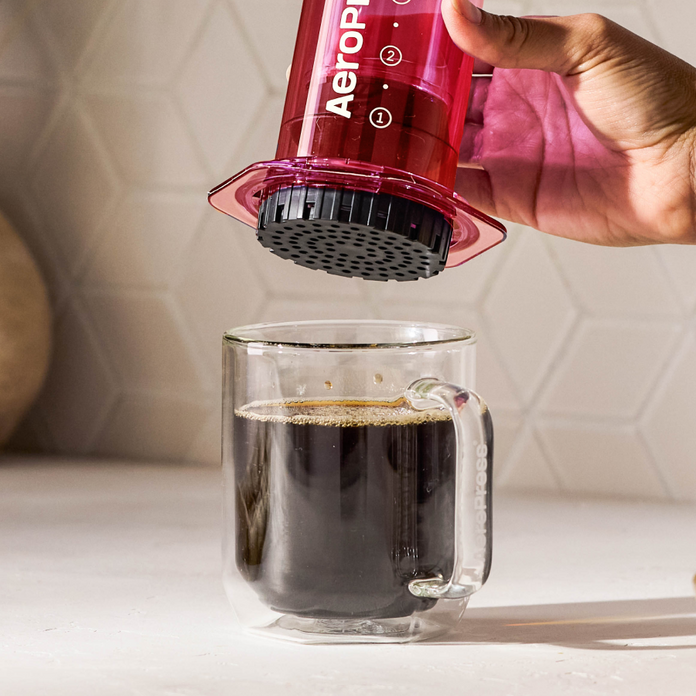 Person using an Aeropress to make coffee in a clear mug.