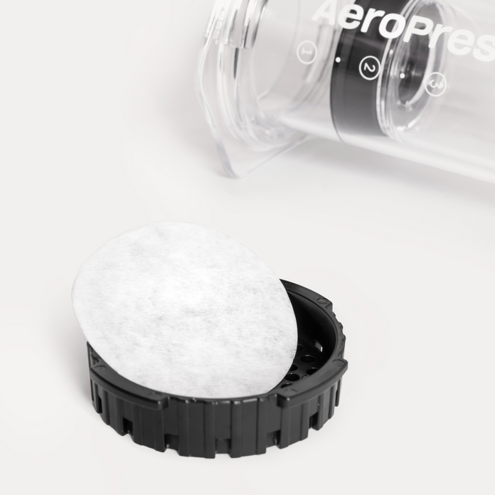 Close-up of a white paper filter in the lid of a coffee brewing device with a clear container and black base on a white background.