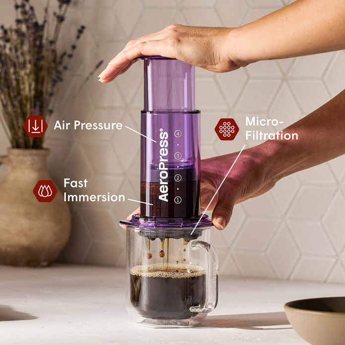 Person using an Aeropress coffee maker with labeled features on a kitchen counter.