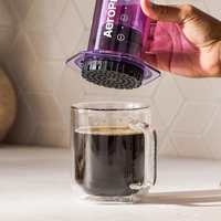 Hand using an Aeropress to make coffee in a clear glass mug.