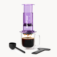 Purple AeroPress coffee maker with a glass mug of coffee and scoop on a white background