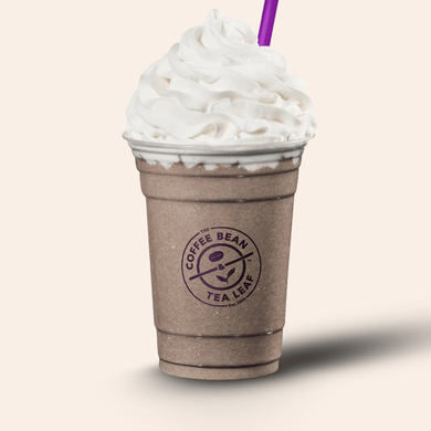 A whipped coffee drink in a brown paper cup with a purple straw, topped with a large swirl of white whipped cream. The cup has a visible Coffee Bean & Tea Leaf logo on the front, set against a solid light beige background.